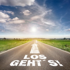 Das Bild zeigt eine Straße mit einem dicken weißen Pfeil, der zum Horizont zeigt. Darunter steht "LOS GEHT'S!"