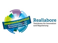 "ausgezeichnet!2022 Bundesministerium für Wirtschaft und Energie" steht auf einem kugelförmigen Logo. Rechts daneben steht: "Reallabore Testräume für Innovation und Regulierung"